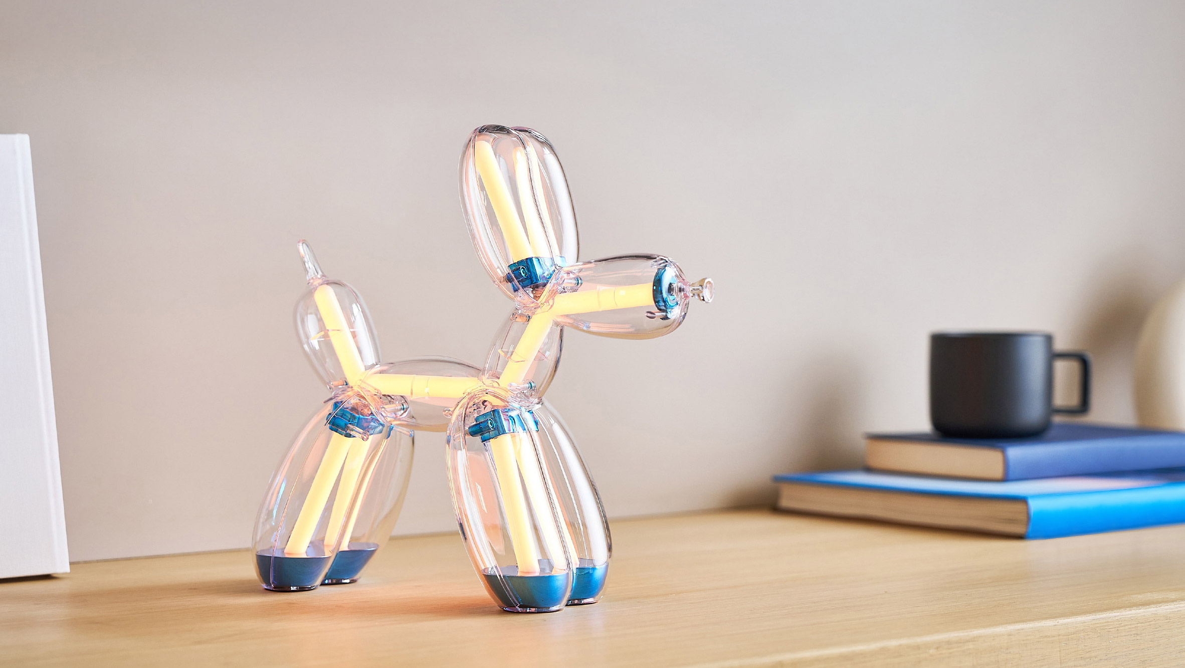 Illuminated Balloon Dog Lamp Chromatic in transparent gold polycarbonate, featuring integrated LED lighting and reflective sculptural form. Official Jeff Koons x Lexon collaboration, presented by Designooor Media and Academy. Written and edited by Hamed Mahzoon